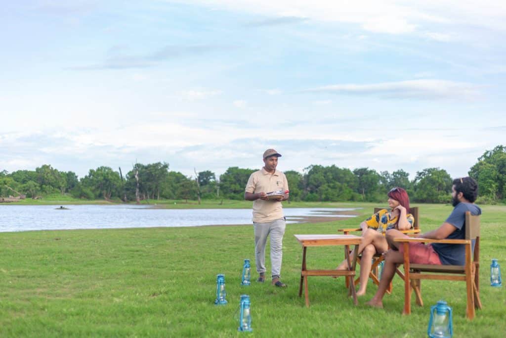 Man serving two people sitting outside by a lake. 