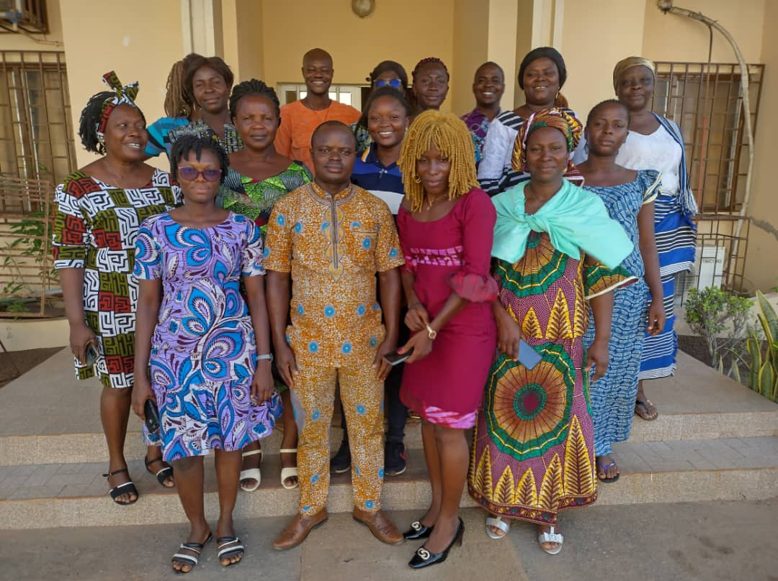 A group of women and men standing together in front of a house in colourful dresses.