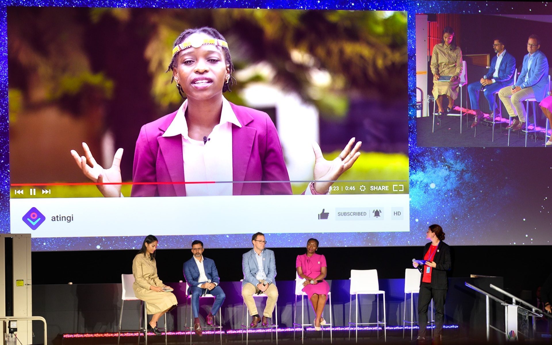 Conference stage with different speakers with video being projected on a screen.