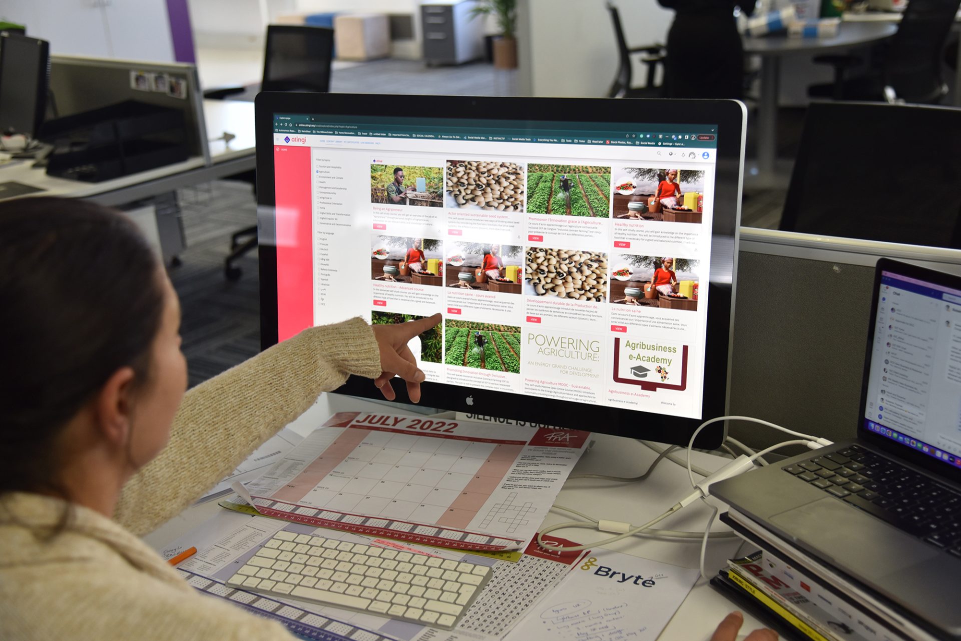 A woman pointing at a desktop computer screen showing the atingi learning platform