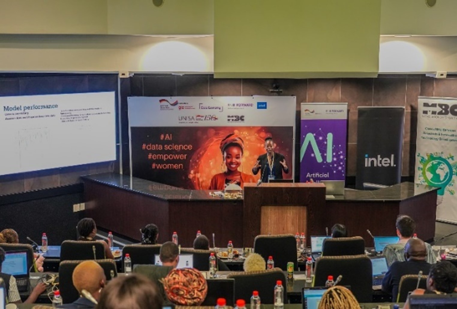 View of auditorium with audience listening to a female speaker on AI topic
