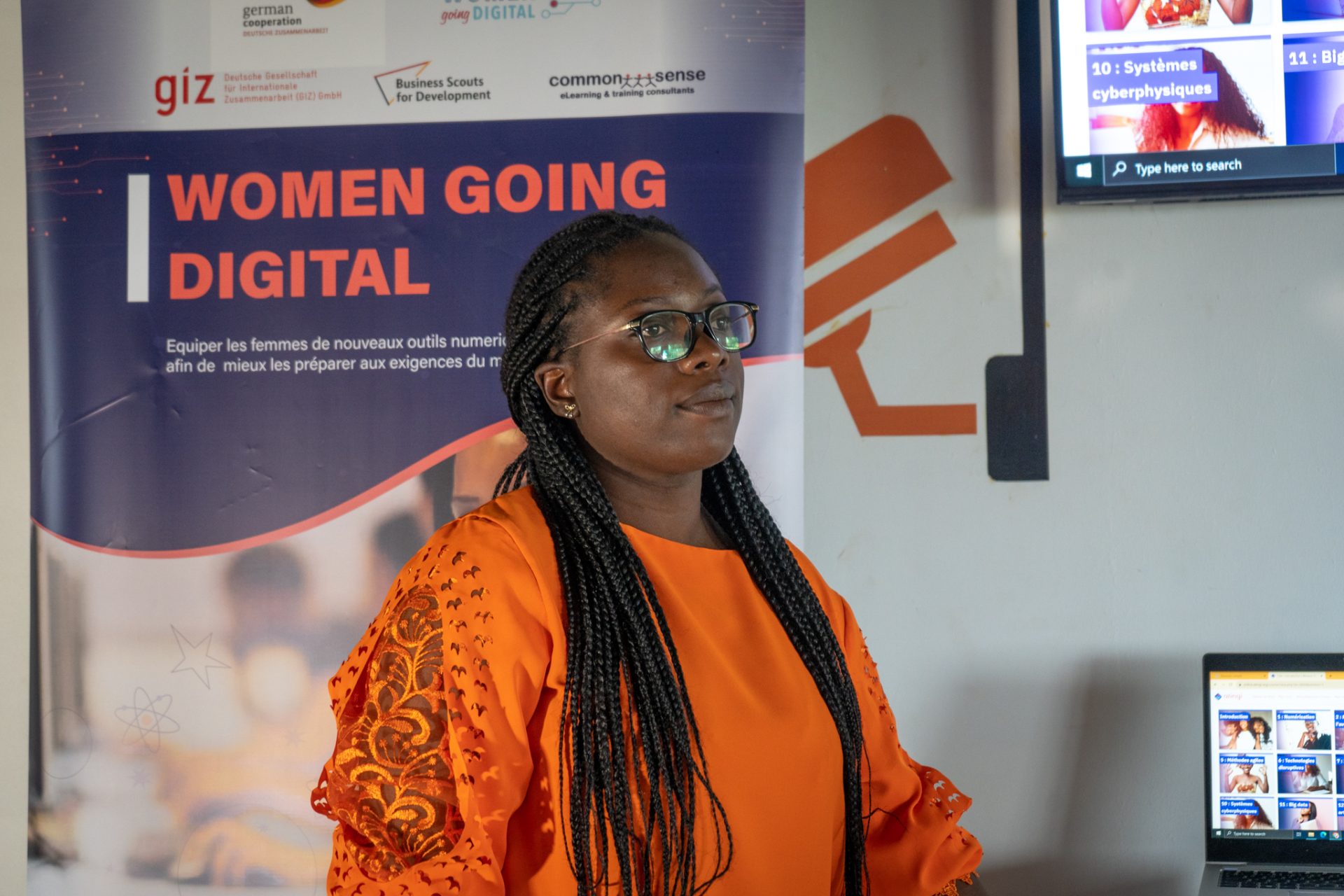 Woman in a orange blouse standing in front of a roll-up banner with the title Women Going Digital